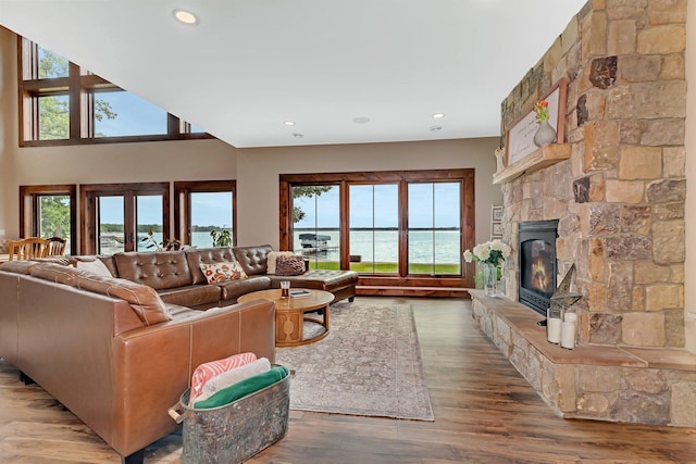 living room featuring a water view, a stone fireplace, hardwood / wood-style flooring, and a healthy amount of sunlight