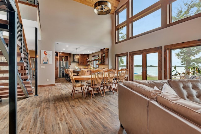 living room featuring a water view, light wood-type flooring, a high ceiling, and french doors