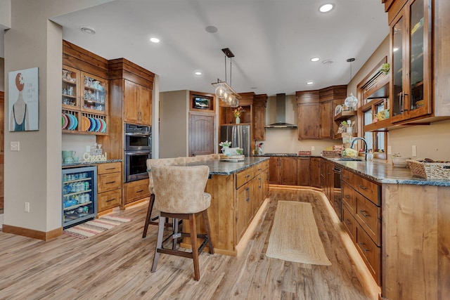 kitchen with pendant lighting, wall chimney exhaust hood, appliances with stainless steel finishes, a kitchen island, and beverage cooler