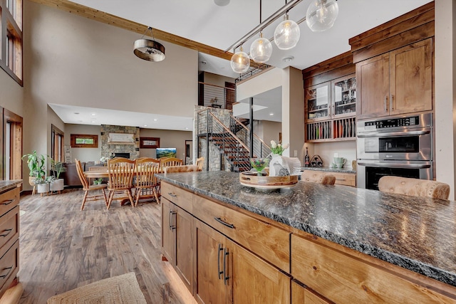 kitchen featuring a stone fireplace, hanging light fixtures, light hardwood / wood-style flooring, dark stone countertops, and stainless steel double oven