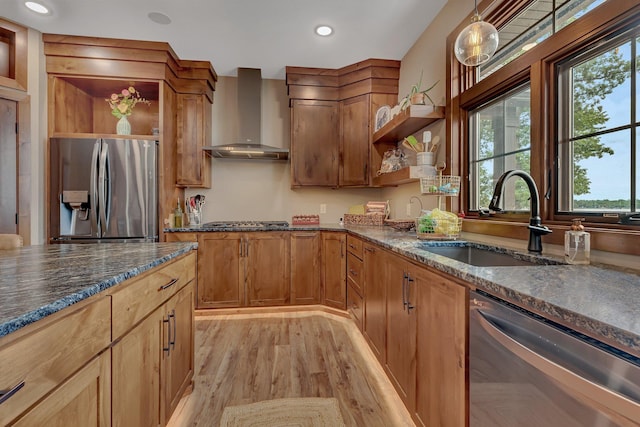 kitchen featuring sink, hanging light fixtures, stainless steel appliances, wall chimney range hood, and light hardwood / wood-style floors