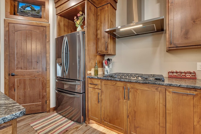 kitchen featuring dark stone countertops, light hardwood / wood-style flooring, stainless steel appliances, and wall chimney range hood