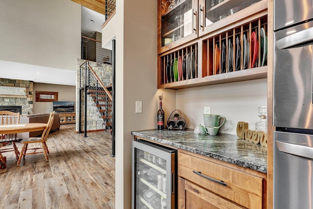 kitchen with beverage cooler, a stone fireplace, light hardwood / wood-style flooring, dark stone countertops, and fridge