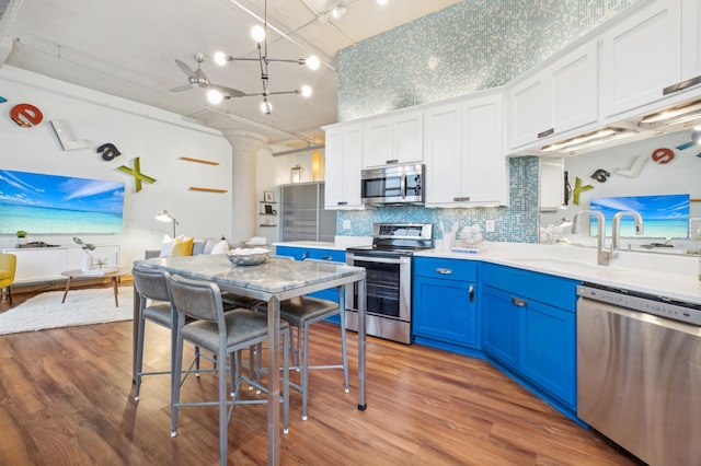 kitchen with blue cabinets, wood finished floors, white cabinets, light countertops, and appliances with stainless steel finishes