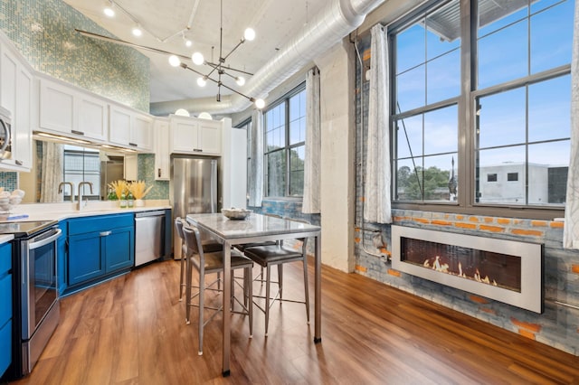 kitchen with appliances with stainless steel finishes, blue cabinetry, wood finished floors, a glass covered fireplace, and white cabinetry