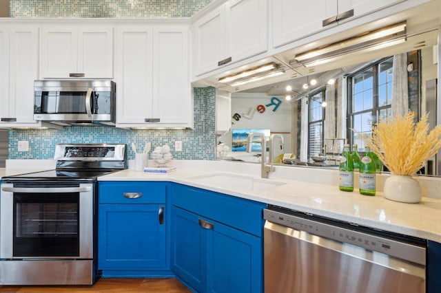 kitchen with stainless steel appliances, a sink, blue cabinetry, white cabinetry, and backsplash