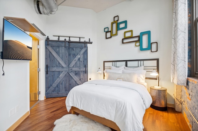 bedroom with wood finished floors, baseboards, and a barn door