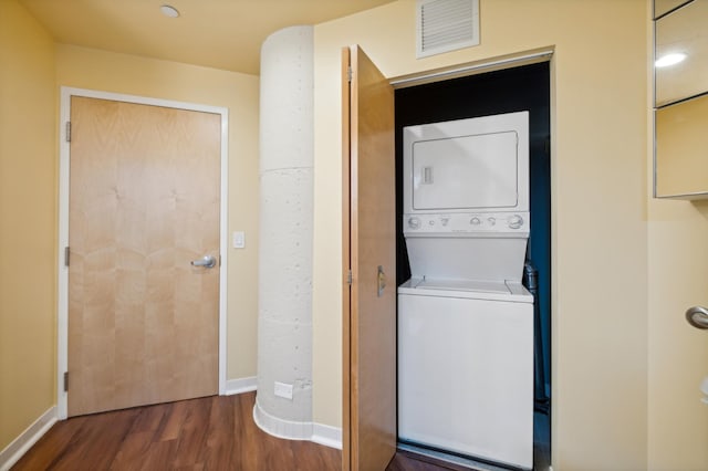 clothes washing area featuring stacked washer / drying machine, wood finished floors, and baseboards