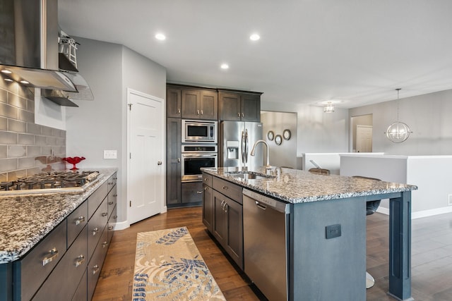 kitchen with sink, decorative backsplash, an island with sink, appliances with stainless steel finishes, and light stone counters