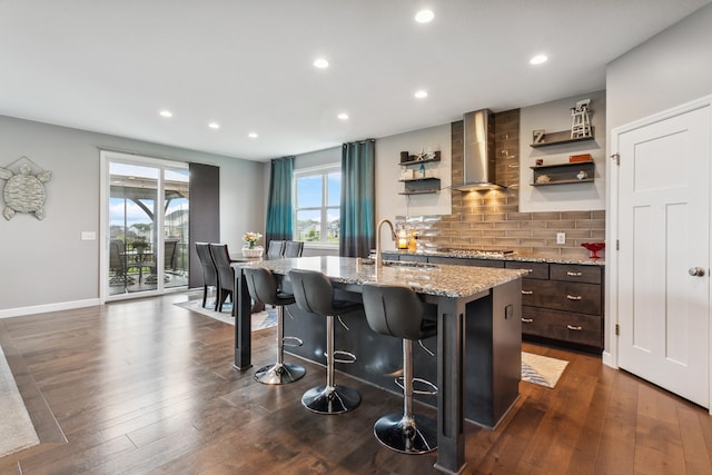 kitchen with wall chimney exhaust hood, a breakfast bar, a kitchen island with sink, dark wood-type flooring, and sink