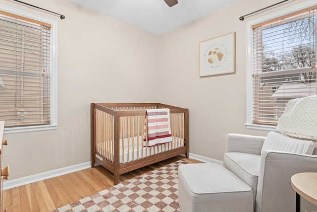 bedroom featuring a crib, wood-type flooring, and ceiling fan