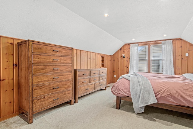 bedroom with lofted ceiling, light colored carpet, a textured ceiling, and wood walls