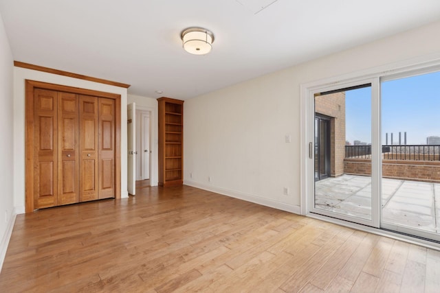 unfurnished bedroom with access to exterior, a closet, baseboards, and light wood-style floors