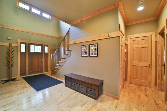 foyer entrance with a towering ceiling, light hardwood / wood-style flooring, a wealth of natural light, and ornamental molding