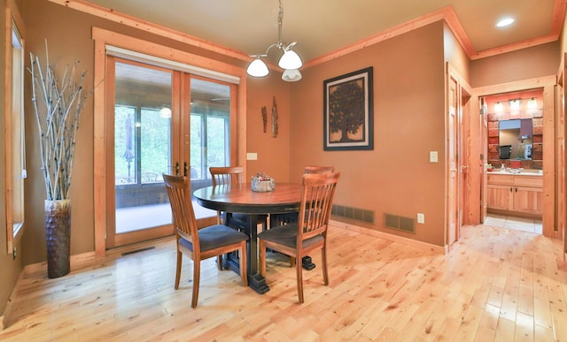 dining room featuring french doors, an inviting chandelier, light hardwood / wood-style flooring, and ornamental molding