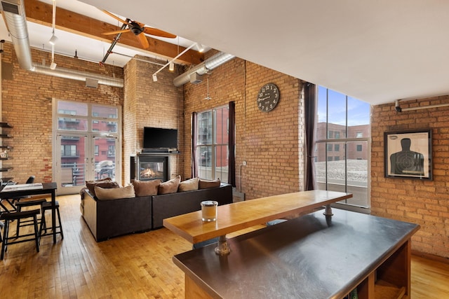 living room with ceiling fan, a wall of windows, brick wall, and light hardwood / wood-style flooring