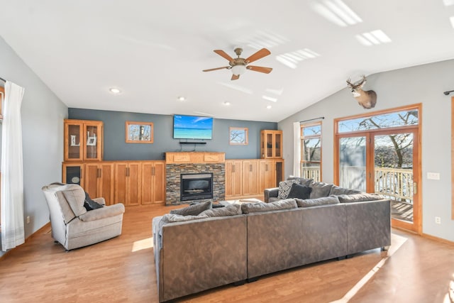 living room featuring ceiling fan, a stone fireplace, light wood-type flooring, and lofted ceiling