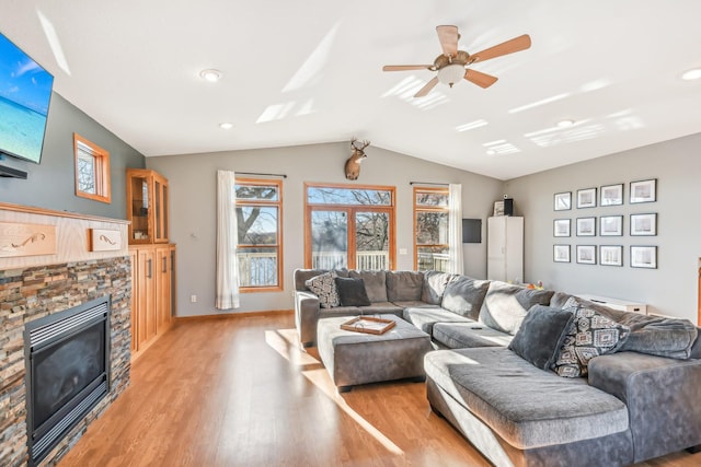 living room featuring ceiling fan, a fireplace, vaulted ceiling, and light wood-type flooring