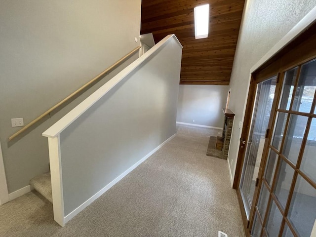 stairway with a brick fireplace, carpet floors, vaulted ceiling, and wooden ceiling