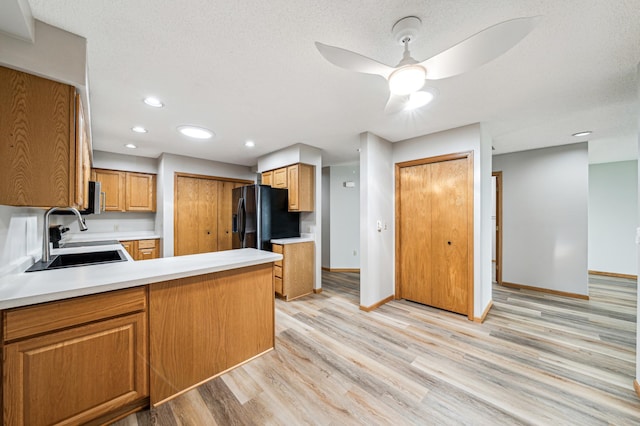 kitchen with kitchen peninsula, black refrigerator with ice dispenser, ceiling fan, sink, and light hardwood / wood-style flooring