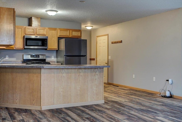 kitchen with dark wood-type flooring, a textured ceiling, light brown cabinets, appliances with stainless steel finishes, and kitchen peninsula