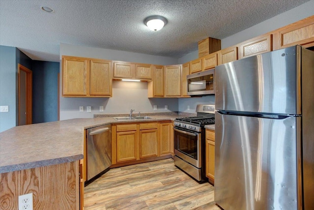 kitchen with light brown cabinetry, sink, light hardwood / wood-style floors, kitchen peninsula, and stainless steel appliances