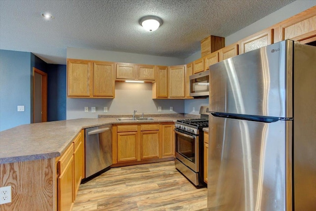 kitchen featuring sink, a textured ceiling, light wood-type flooring, kitchen peninsula, and stainless steel appliances