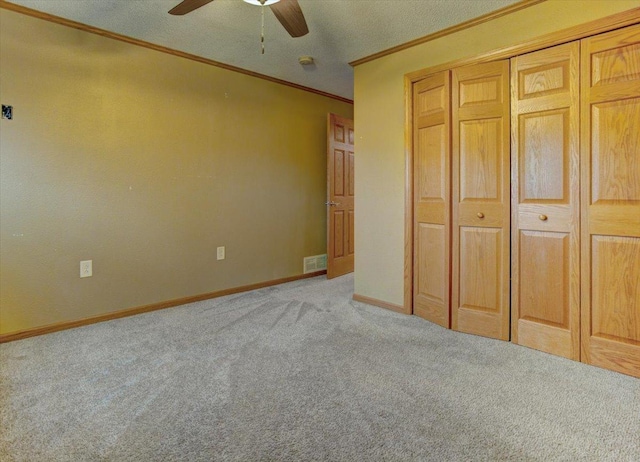 unfurnished bedroom featuring ornamental molding, light colored carpet, ceiling fan, a textured ceiling, and a closet