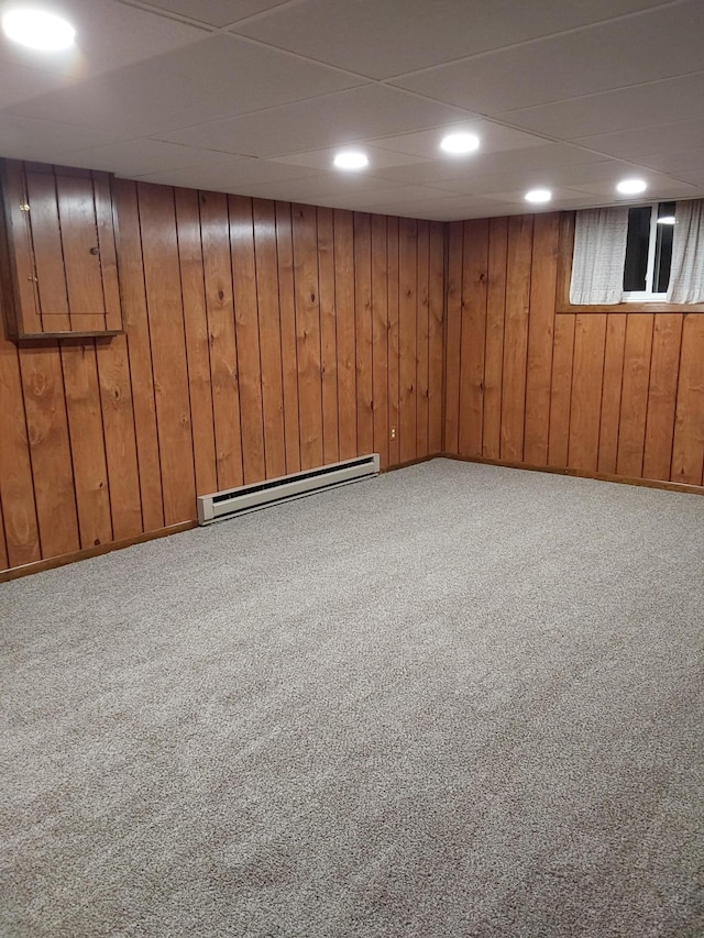 basement featuring carpet flooring, wooden walls, and a baseboard heating unit