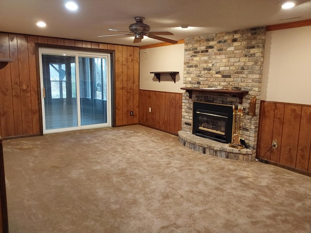 unfurnished living room with ceiling fan, wood walls, light carpet, and a brick fireplace