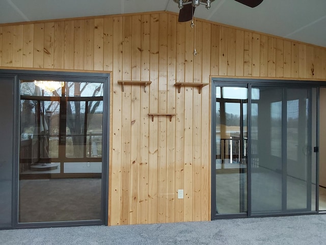 entryway featuring wood walls, carpet floors, a healthy amount of sunlight, and vaulted ceiling