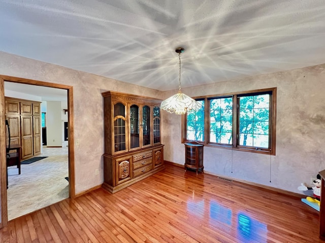 unfurnished dining area featuring an inviting chandelier and light hardwood / wood-style flooring