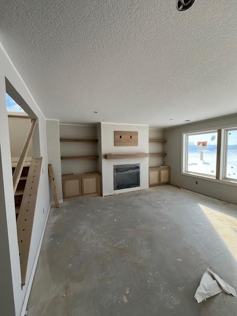 unfurnished living room featuring a textured ceiling, a fireplace, and unfinished concrete flooring