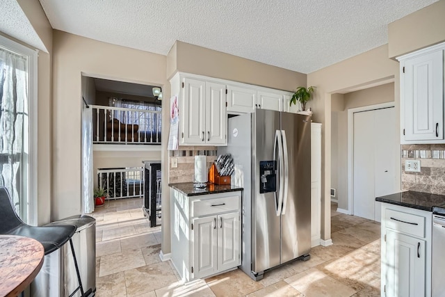 kitchen with decorative backsplash, stainless steel fridge, dark stone counters, a textured ceiling, and white cabinetry