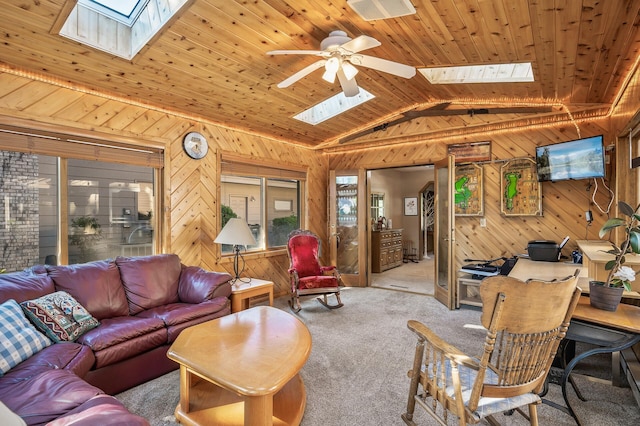 carpeted living room featuring vaulted ceiling with skylight, ceiling fan, wood ceiling, and wooden walls