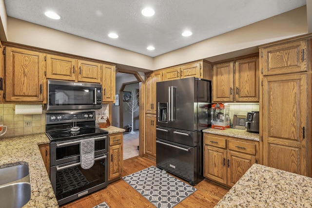 kitchen with decorative backsplash, light hardwood / wood-style floors, light stone counters, and stainless steel appliances