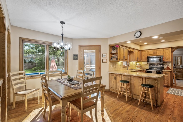 dining space with a textured ceiling, wood-type flooring, sink, and a chandelier