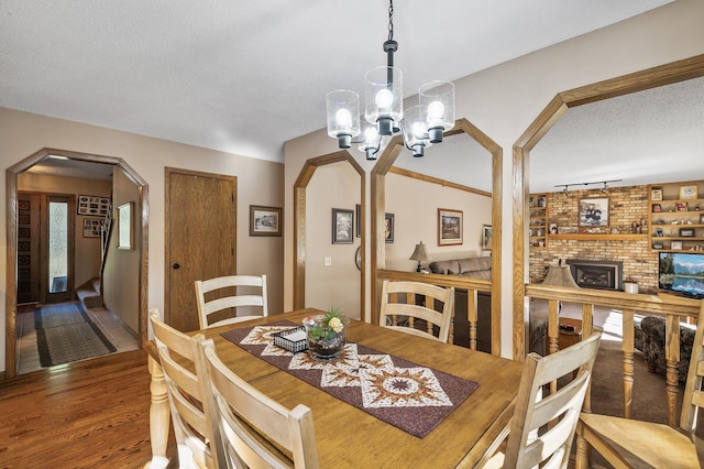 dining room with a brick fireplace, a notable chandelier, wood-type flooring, track lighting, and a textured ceiling