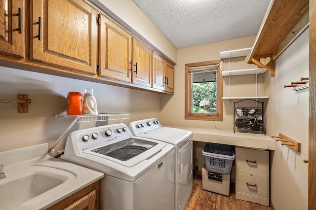 laundry area featuring hardwood / wood-style floors, cabinets, sink, washing machine and dryer, and a textured ceiling