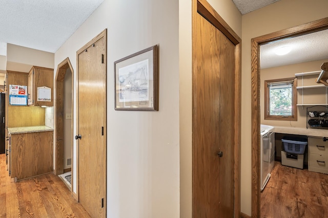 corridor featuring washing machine and dryer, a textured ceiling, and light wood-type flooring