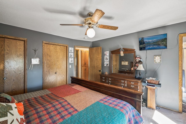 carpeted bedroom with ceiling fan, a textured ceiling, and two closets