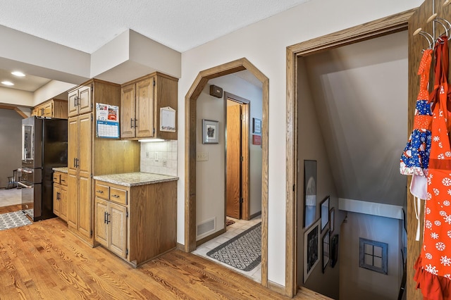 kitchen featuring light stone countertops, light hardwood / wood-style floors, a textured ceiling, decorative backsplash, and black refrigerator