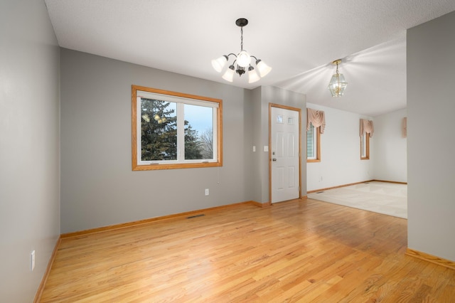 spare room featuring a notable chandelier, a textured ceiling, and light hardwood / wood-style flooring