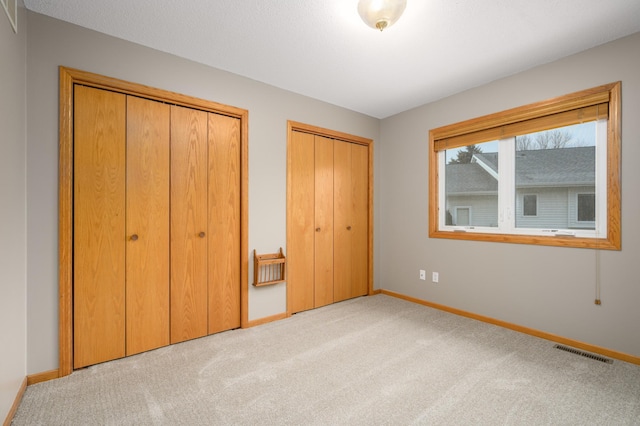 unfurnished bedroom featuring light colored carpet and multiple closets