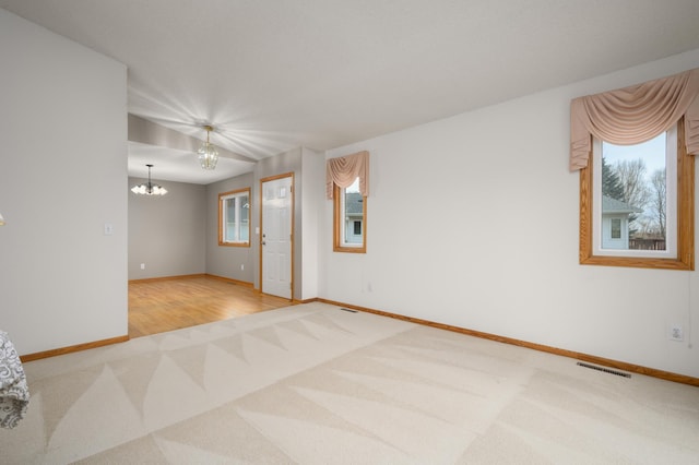 carpeted spare room featuring a chandelier, visible vents, and baseboards