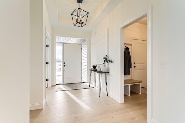 entrance foyer featuring light hardwood / wood-style floors, a tray ceiling, and a notable chandelier