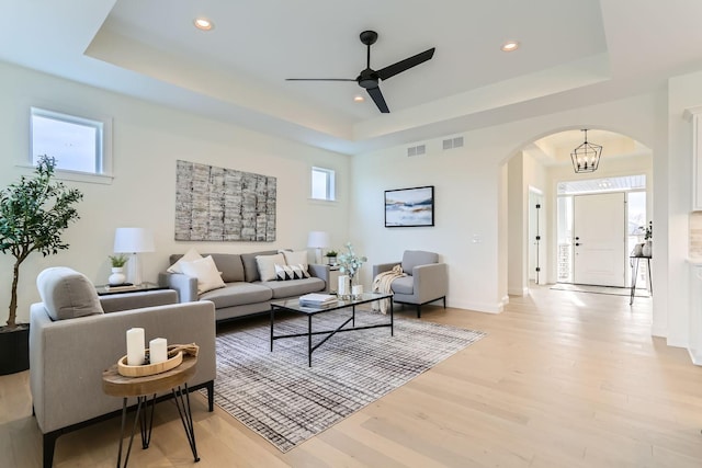 living room featuring light hardwood / wood-style floors, a raised ceiling, and ceiling fan