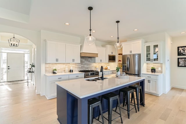 kitchen with white cabinetry, sink, stainless steel appliances, decorative light fixtures, and a kitchen island with sink