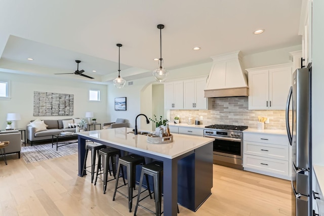 kitchen with white cabinets, a kitchen island with sink, appliances with stainless steel finishes, and custom exhaust hood