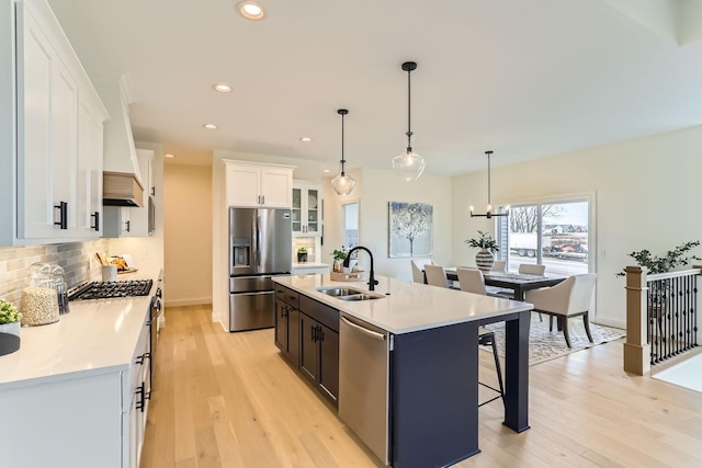 kitchen with a kitchen island with sink, white cabinets, hanging light fixtures, sink, and stainless steel appliances